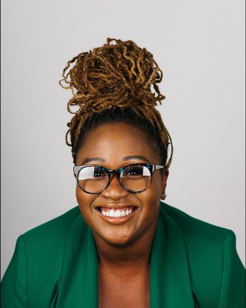 kenya, smiling in a green blazer and tortoiseshell glasses